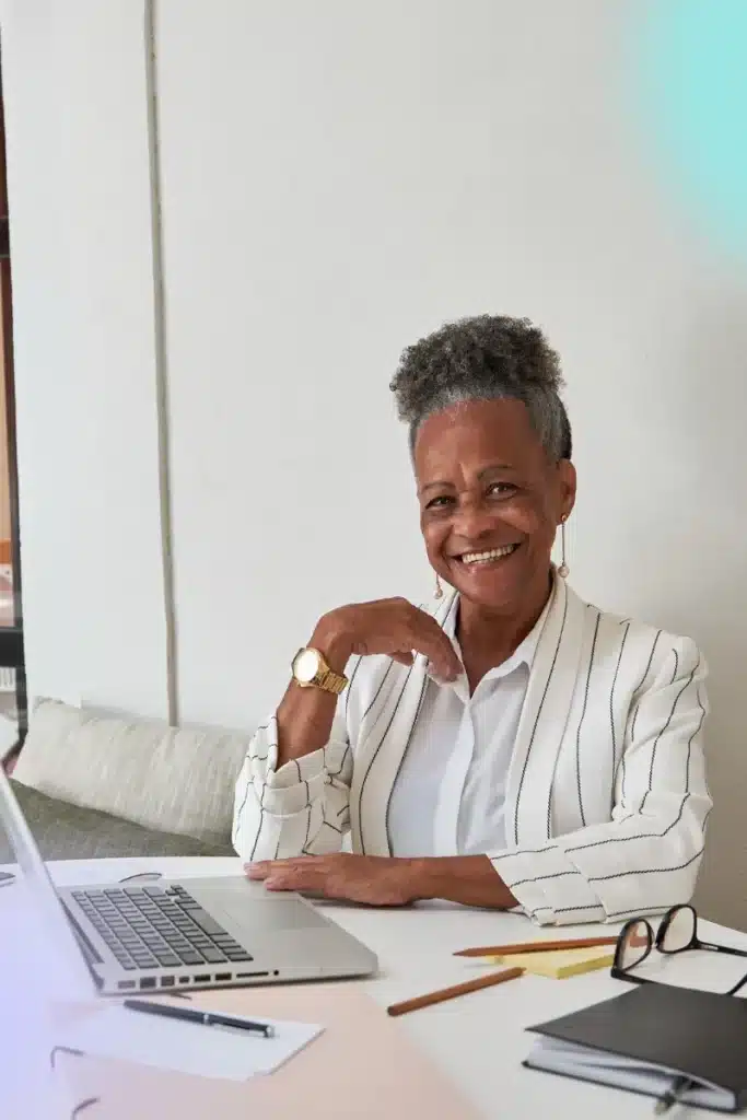 Black female business person smiling at a table with a laptop